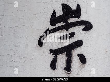Chinese character painted on a cracked white wall in a quiet urban area during daylight hours Stock Photo