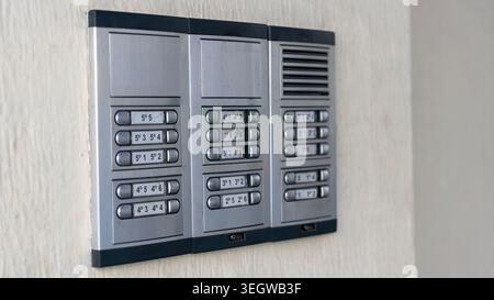 Close up of apartment building intercom system with multiple doorbell buttons mounted on white wall indoors. Stock Photo