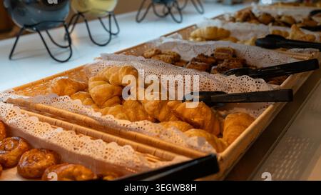 Fresh croissants and assorted pastries served on buffet table in hotel restaurant during breakfast with warm cozy lighting. Stock Photo