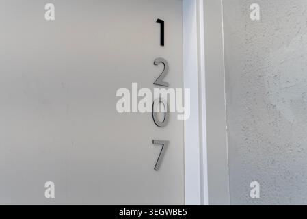 Close up of modern hotel room number 1207 on white door in resort or apartment corridor with minimalist interior design. Stock Photo