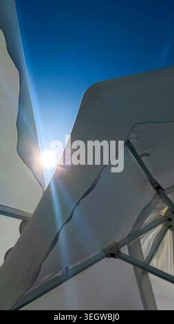 Sunlight shining through the fabric of a white canopy, revealing a blue sky and creating a lens flare effect in a bright outdoor setting Stock Photo