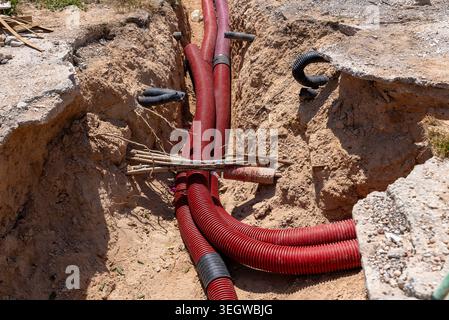 Red corrugated utility pipes installed underground in construction trench for electrical or communication infrastructure. Stock Photo