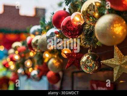 Bright red, gold, and silver Christmas ornaments hang on green garland, illuminated by warm lights. Stock Photo