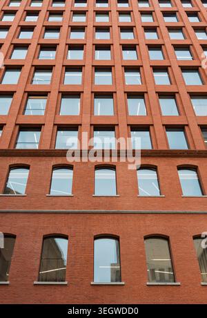 Rising view of a contemporary brick building featuring a grid of many square windows and arched windows on a lower level Stock Photo