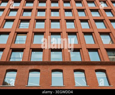 Rising view of a contemporary brick building featuring a grid of many square windows and arched windows on a lower level Stock Photo