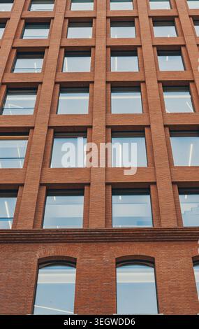 Rising view of a contemporary brick building featuring a grid of many square windows and arched windows on a lower level Stock Photo
