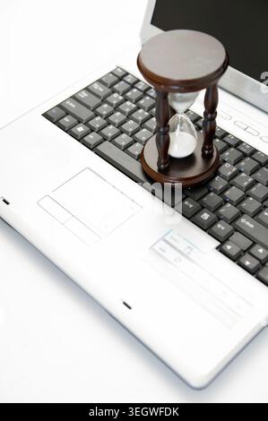 A small hourglass sits on a laptop keyboard, indicating a need for time management in a digital work setting. Stock Photo