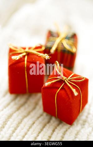 A row of vibrant red gift boxes with golden bows are nestled on a white, knitted blanket. Stock Photo