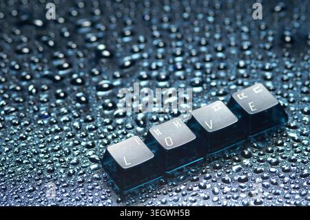 A close-up of a keyboard key layout with the word "LOVE" spelled out, lying on a wet, dark surface. Stock Photo