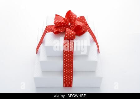 A stack of three white gift boxes wrapped in red ribbon and tied with a bow, sitting on a white surface. Stock Photo