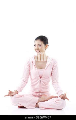 A woman in a pink outfit sits in a lotus position, her hands in a meditative pose, against a white background. Stock Photo