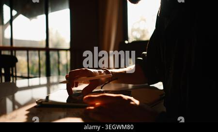 Man creating digital art on tablet using stylus, focusing on work at sunset Stock Photo