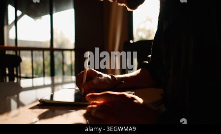 Man creating digital art on tablet using stylus in sunlit home office Stock Photo