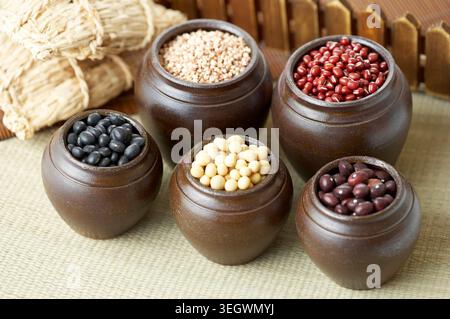 A selection of various types of beans in clay pots, arranged on a woven tablecloth. Stock Photo