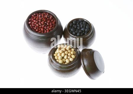 Three small clay pots filled with red, white, and black beans, arranged on a plain white background. Stock Photo