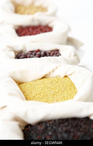 A row of fabric bags filled with different types of grains and beans, arranged on a white surface. Stock Photo