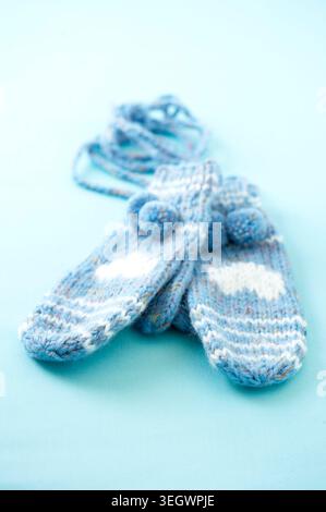 A pair of knitted baby blue and white baby booties with pom-poms on a light blue background. Stock Photo