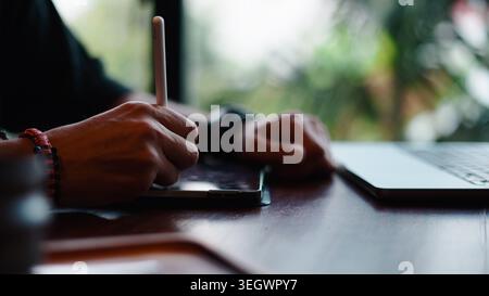 Artist hands creating digital art on tablet using stylus next to laptop screen Stock Photo