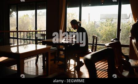 Man working remotely in cafe, sitting by window with sunlight streaming Stock Photo