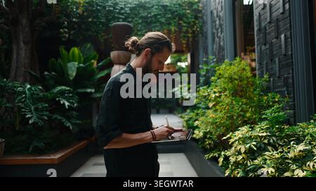 Man digital artist creating artwork on tablet in green tropical garden Stock Photo