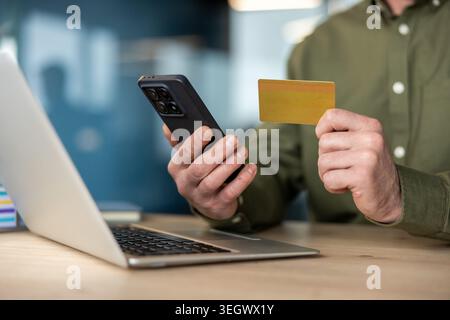 Man holding a smartphone and a credit card, processing an online payment or digital banking transaction at a laptop, representing e-commerce, mobile s Stock Photo