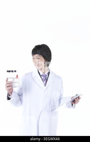 A young doctor in a lab coat holds a test tube rack and a clipboard, examining samples in a laboratory setting. Stock Photo