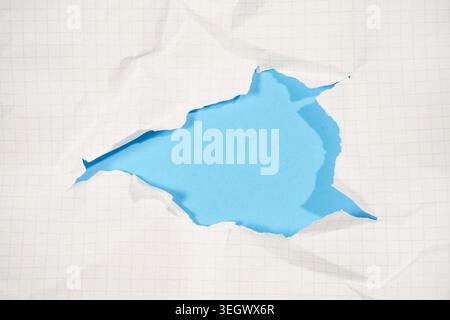 Several blue torn paper pieces scattered on white grid notebook background showing various tearing patterns and irregular edges creating textural comp Stock Photo