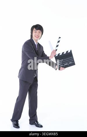 A young Asian businessman in a suit is holding a clapperboard on a white background. Stock Photo