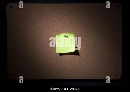 A bright green sticky note is stuck to a dark brown bulletin board with a single pushpin. Stock Photo