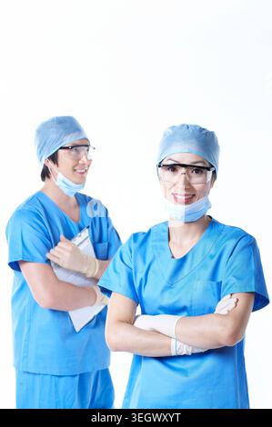 Two surgeons in blue scrubs, wearing masks, standing in a hospital corridor, smiling. Stock Photo