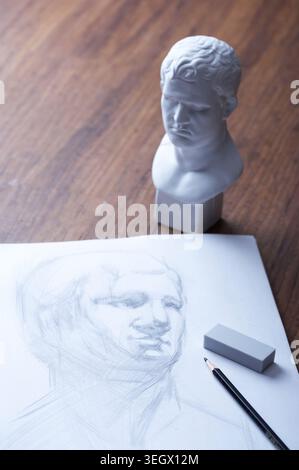 A still life of a sketch of a classical bust, with a few art tools on a wooden table. Stock Photo