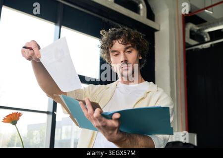 A handsome young man focuses on files while standing by a bright window in an office setting. Stock Photo