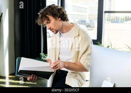 A handsome young man focused on reviewing documents while seated at a stylish office desk Stock Photo