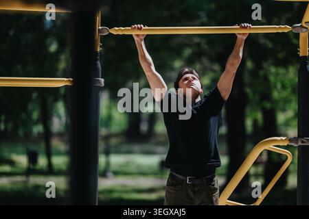 Man doing pull-ups on yellow bar in park outdoor workout for strength training and fitness Stock Photo