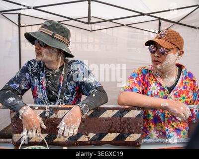 Two men covered in white powder celebrate the Songkran festival in Lampang, Thailand, wearing colorful shirts and sunglasses. Stock Photo