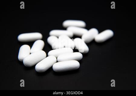White prescription pills scattered on a black background, creating a clean medical, pharmaceutical, and healthcare-themed image. Stock Photo
