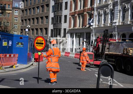 Construction workers in high visibility clothing manage traffic with stop sign during roadworks in the City of London urban street setting. Stock Photo