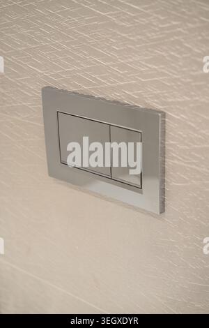 Chrome dual flush plate with two rectangular buttons mounted on a light textured wall, providing a sleek, modern, and water-efficient solution for Stock Photo