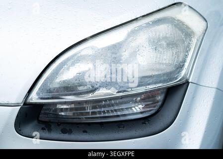 Close-up of a foggy car headlight covered in water droplets on a silver vehicle  Stock Photo