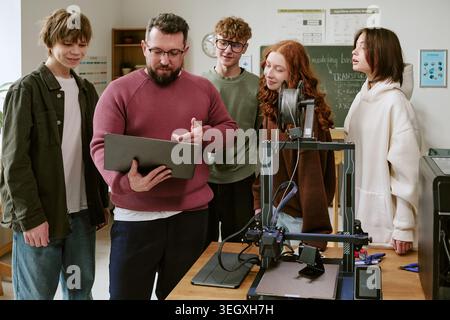 Male Teacher Guiding Teenagers Using 3d Printer in Stem Classroom Stock Photo
