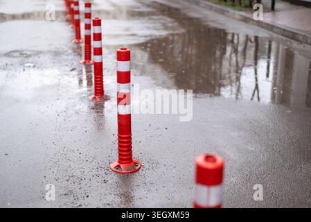 Red and white striped flexible traffic bollards on a wet asphalt road with puddles. Stock Photo