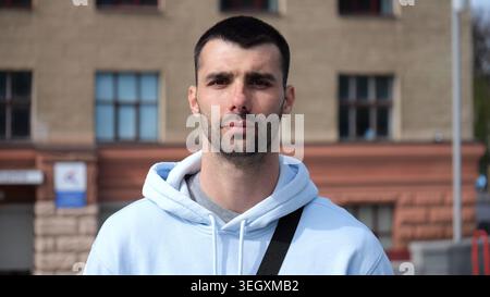 Portrait of young confident bearded man in casual clothing with cityscape background. Close up of handsome guy looks into camera standing at city Stock Photo