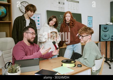 Teacher Guiding Teenagers Using 3d Printing Tools in Classroom Stock Photo