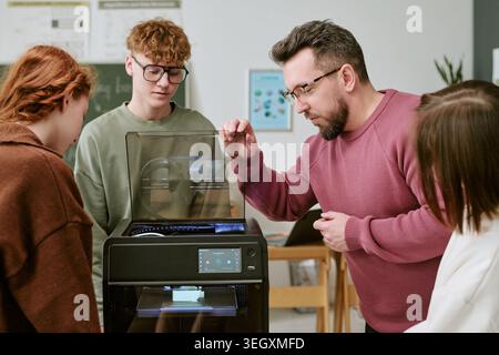 Teacher Guiding Teenagers Using 3d Printer in Classroom Stock Photo