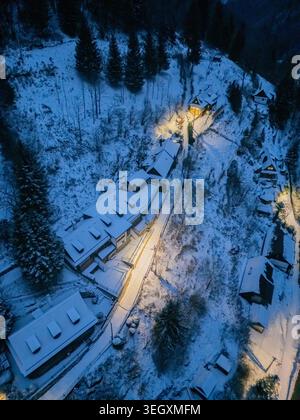 Aerial view of the historic village of Spania Dolina with snow-covered roofs and glowing lights nestled among pine trees at dusk Spania Dolina, Banska Stock Photo