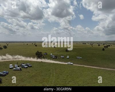 Aerial view of a rally car racing on a dirt track kicking up dust across the vast savanna of Swara Plains Conservancy with spectators and parked vehic Stock Photo