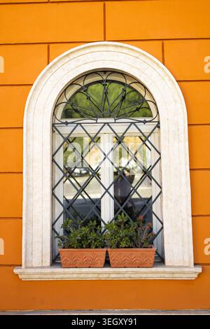Beautiful arched window with decorative wrought iron grate on vibrant orange wall Mediterranean style building exterior. Stock Photo