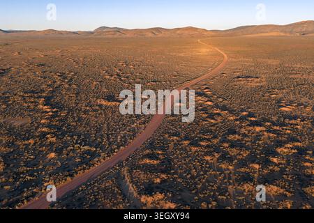 Aerial view of a winding dirt road stretching through the vast arid outback landscape with rolling hills during golden hour in Flinders Ranges, South Stock Photo
