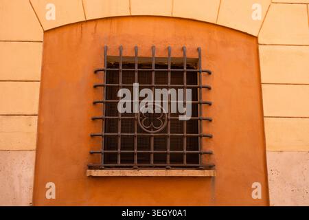 Symmetric arched window with decorative iron grate on vibrant orange stucco wall. Stock Photo