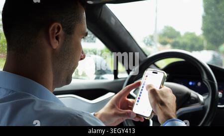 Male entrepreneur browsing modern smartphone while riding autonomous self driving electric car at city. Successful businessman using phone during Stock Photo